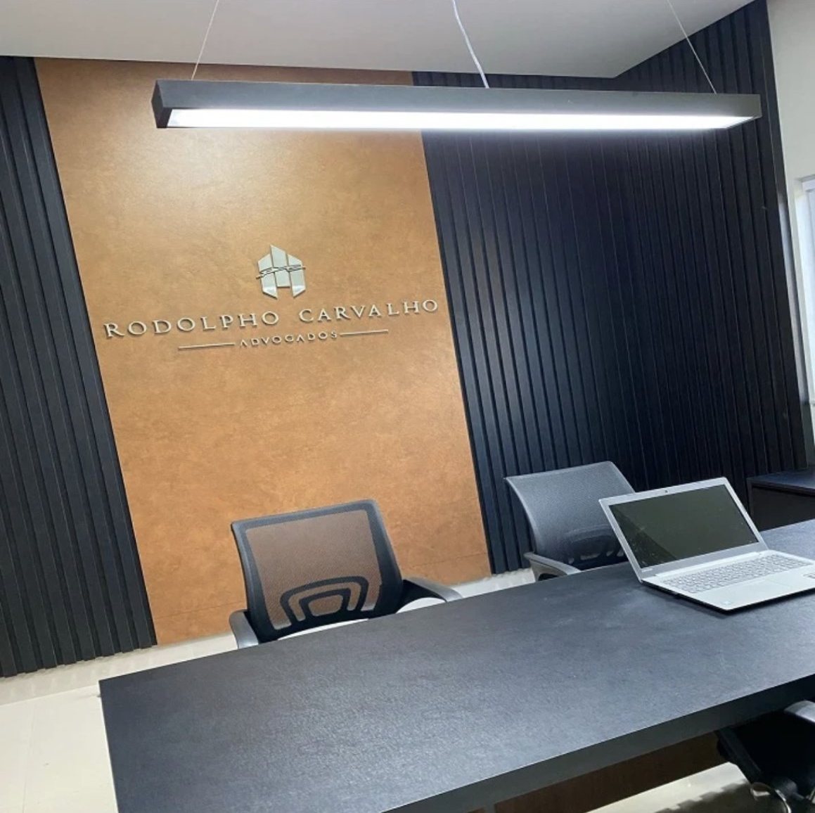 Sala de reunião com parede cobre, ripado preto, letreiro em aço e mesa preta